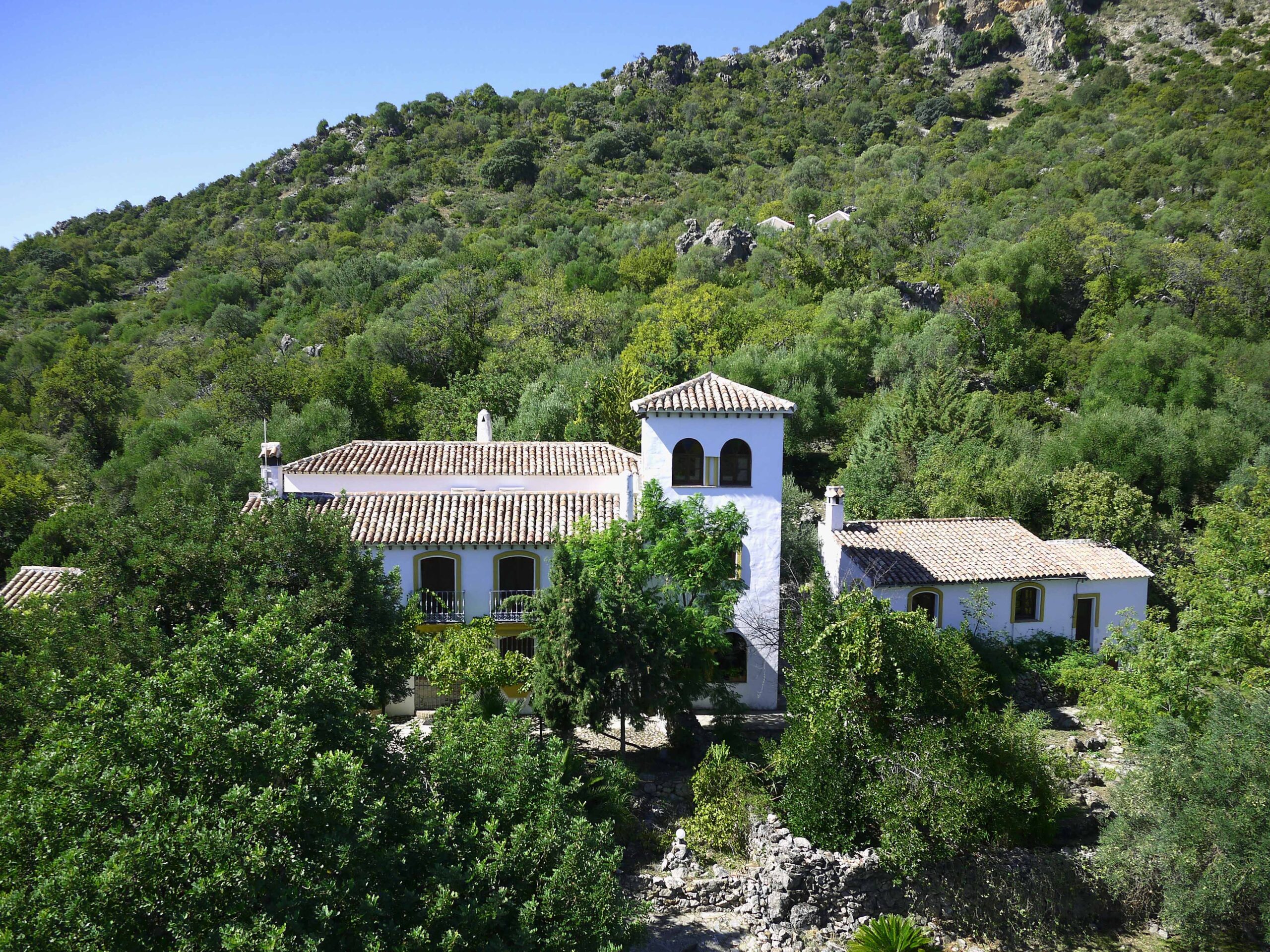 White Andalusian villa with terracotta roofs nestled in a lush green mountainside, Spain.