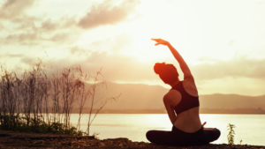 Woman demonstrating spinal core stability in seated yoga lateral flexion pose by lake at sunset