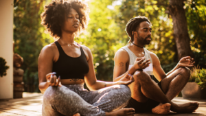 Two people practicing mindfulness meditation outdoors in a cross-legged seated pose, demonstrating the neurodevelopmental sequence in yoga through grounded, floor-based posture and breath awareness