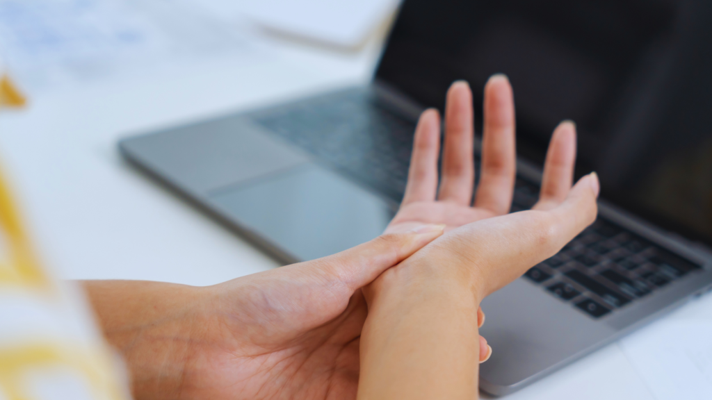 Person holding their wrist showing pain and discomfort from Carpal Tunnel Syndrome while using a laptop