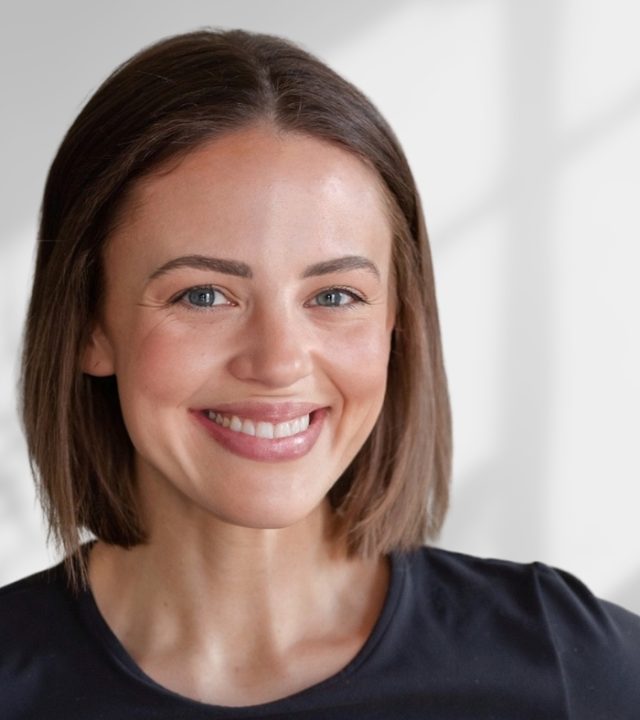 Smiling woman with a brown bob haircut wearing a black top in a professional headshot.